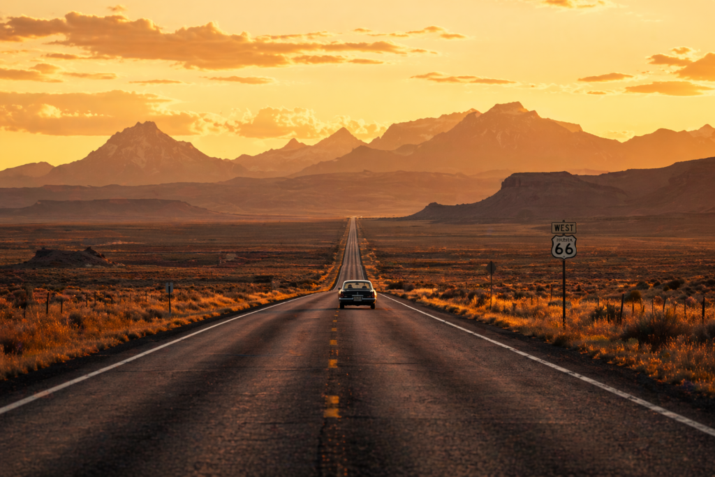 Scenic open road through the American West with mountains and golden sunset — best road trips USA